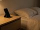Chambre calme en soirée avec un smartphone posé à distance sur une commode, un lit sobre et une lumière chaude tamisée.